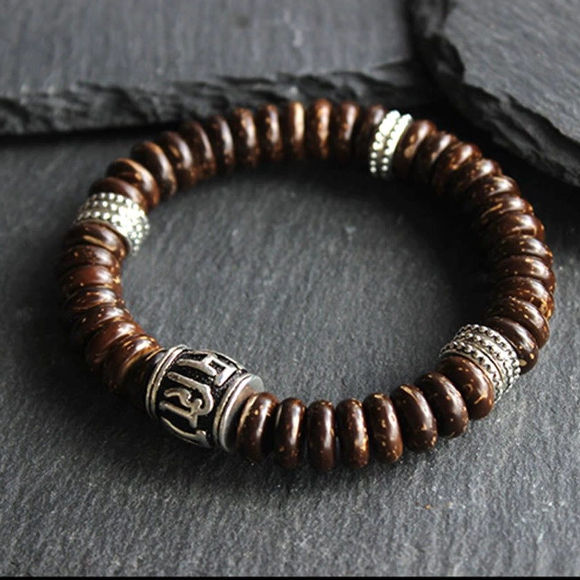 Top-down flat lay of brown coconut shell Om Mani Padme Hum bracelet with silver metal spacers on dark stone background