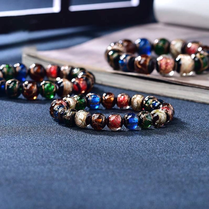 Multiple assorted Buddhist glass bead bracelets arranged on books and fabric showing color variations