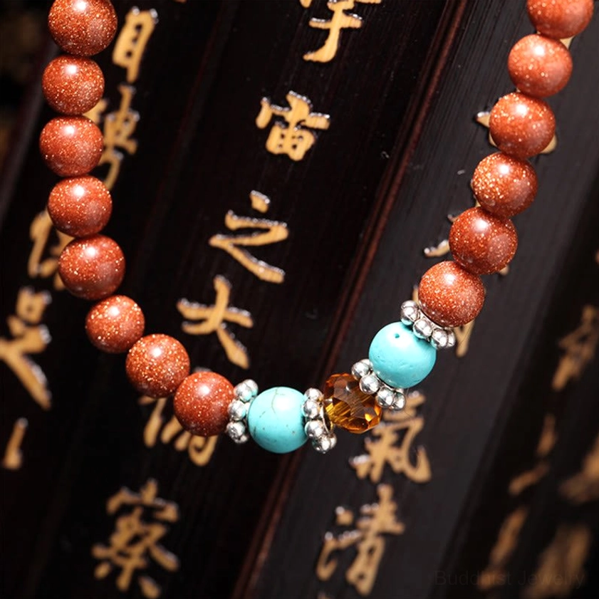 Full 108-bead goldstone mala strand laid flat with matching decorative bead accessories on Chinese calligraphy wooden board