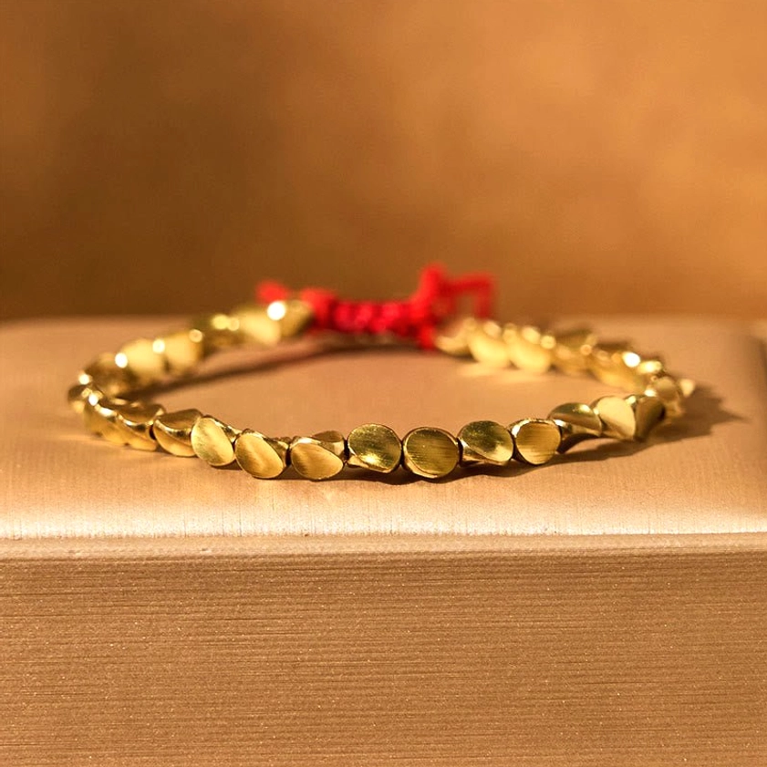 Oval copper beads bracelet with red tassel on wooden display box, highlighting artisanal handcrafted quality and matte brass texture