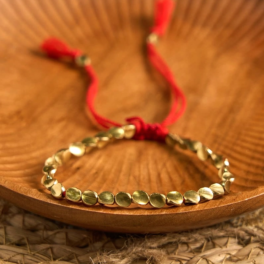 Round flat copper bead bracelet with red hanging tassel cords on woven mat, showing braided closure for meditation practice