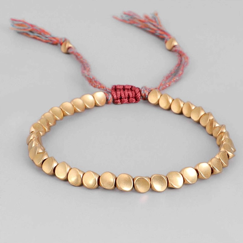 Minimalist flat copper bead bracelet with smooth round light gold beads and mixed-color woven cord with tassels on light pink background