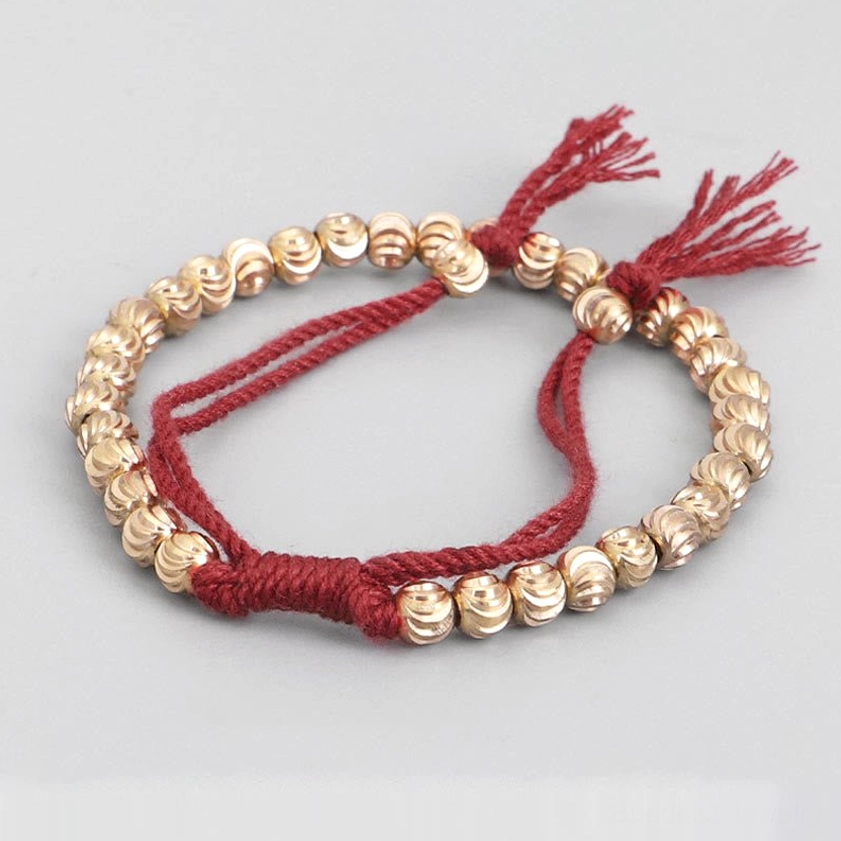 Handmade copper bead bracelet with red cotton cord and ridged gold beads, oblique angle showing craftsmanship