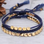 Three handmade copper beaded bracelets with adjustable woven nylon cord displayed on wooden surface with natural decor