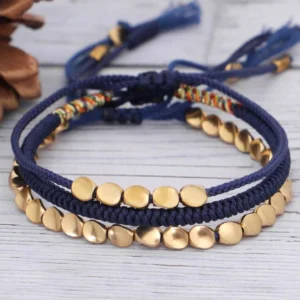 Three handmade copper beaded bracelets with adjustable woven nylon cord displayed on wooden surface with natural decor