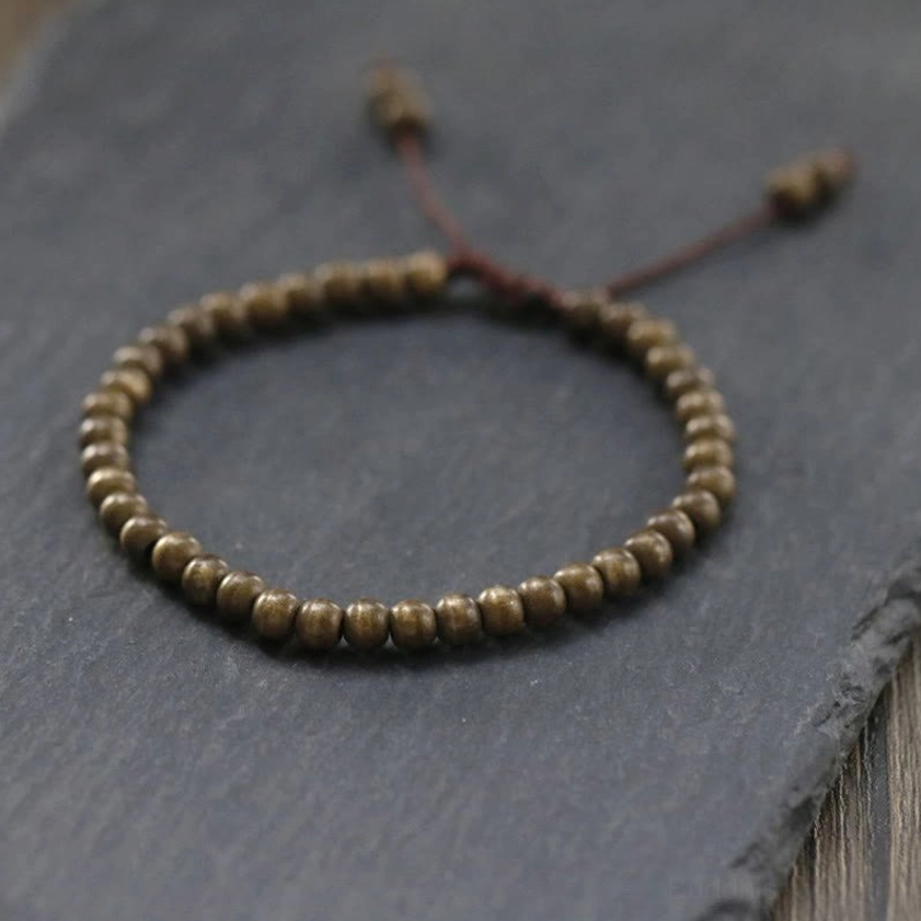 Minimalist copper bead bracelet flat lay on dark wood and slate, adjustable drawstring design for prosperity and balance