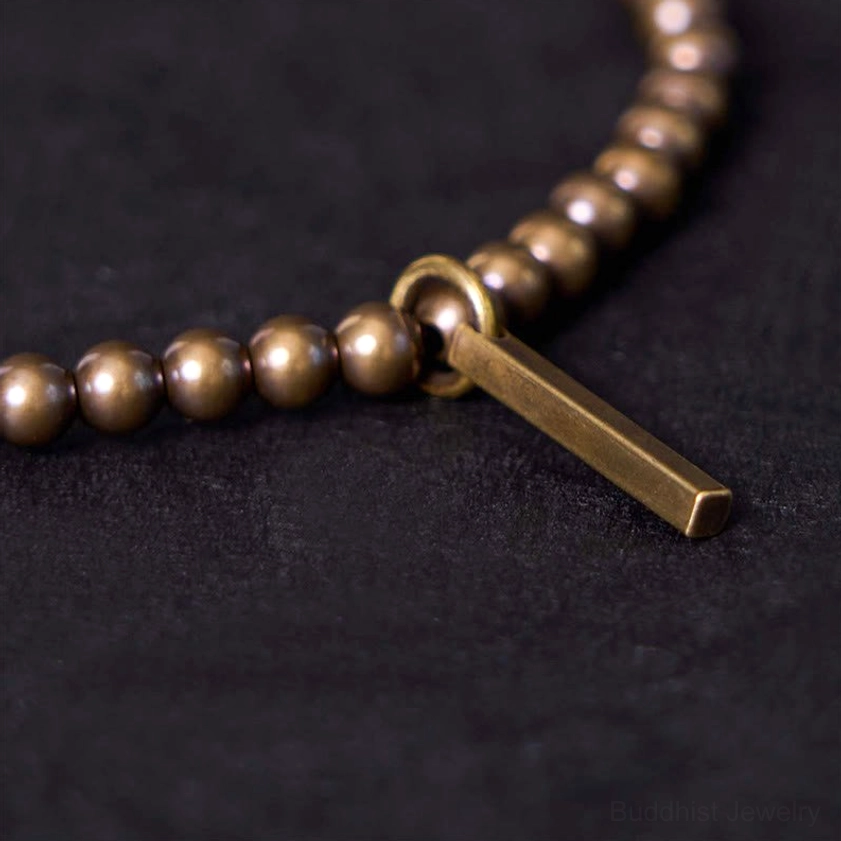 Macro close-up side view of polished copper brass beads and rectangular bar pendant with matte bronze texture