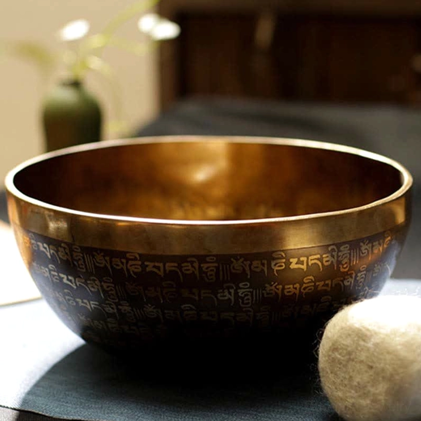 Copper singing bowl front overhead view with engraved Tibetan Buddhist scriptures and wooden mallet