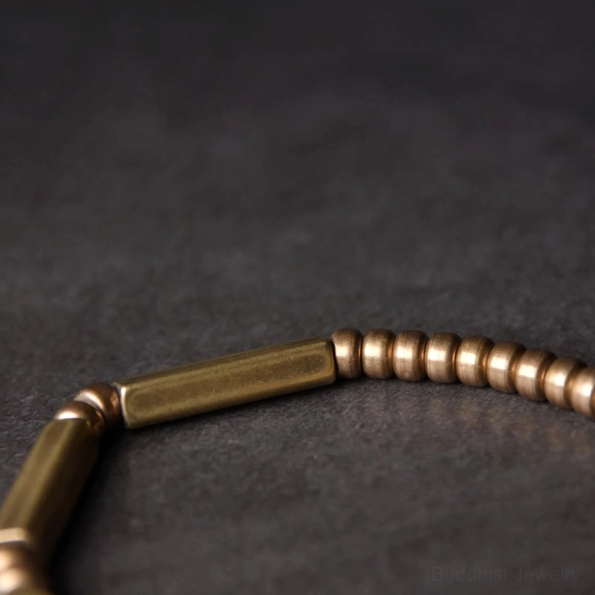 Macro close-up of copper bracelet beads, alternating round and cylindrical metal elements with warm metallic finish