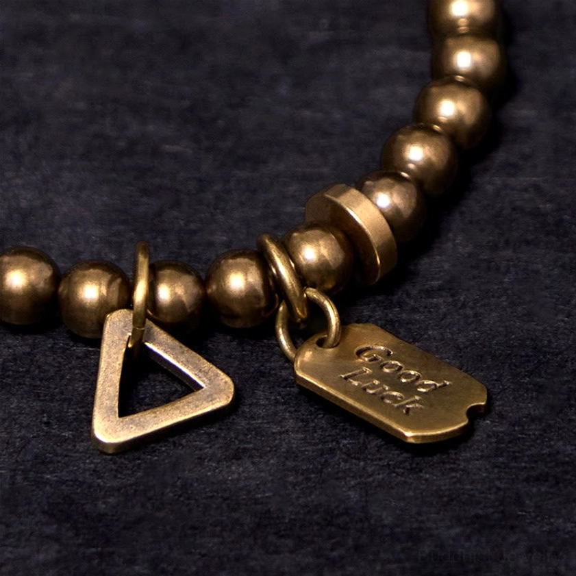Close-up detail of copper bracelet hardware showing engraved Good Luck text and metal bead craftsmanship
