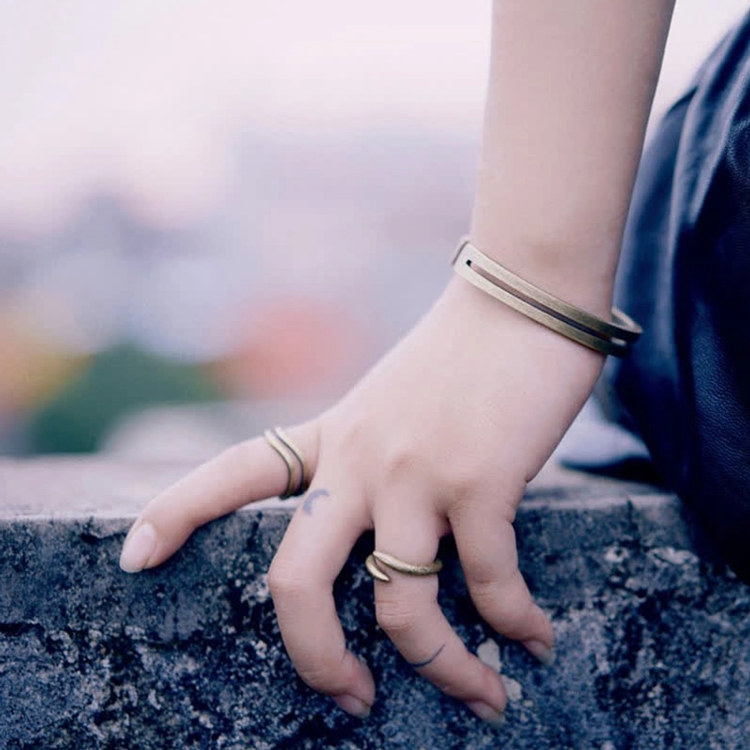 Styled copper cuff bracelet worn on wrist with matching thin rings in outdoor casual setting
