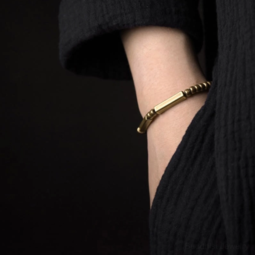 Copper bracelet worn on wrist partial side view, low-profile antique brass tone with black clothing background