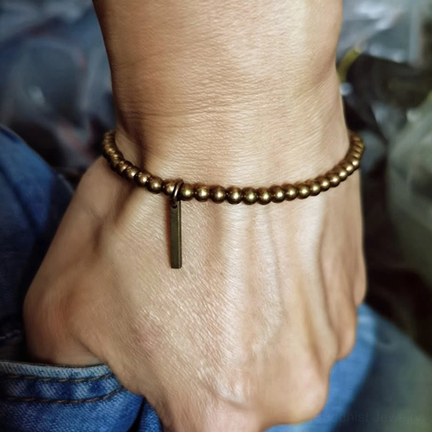 Copper brass beaded Buddhist bracelet worn on male wrist with denim clothing background, showing slim comfortable fit
