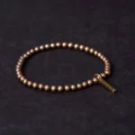 Copper brass beaded Buddhist bracelet with rectangular pendant charm in antique bronze finish, displayed in flat lay against dark fabric backdrop
