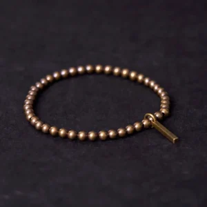 Copper brass beaded Buddhist bracelet with rectangular pendant charm in antique bronze finish, displayed in flat lay against dark fabric backdrop