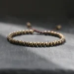 Copper brass beads bracelet with brown tassel cord on dark slate surface, high angle view showing round 5mm polished beads