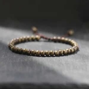 Copper brass beads bracelet with brown tassel cord on dark slate surface, high angle view showing round 5mm polished beads
