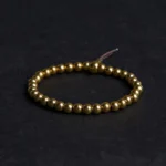 Copper brass Buddhist beaded bracelet with golden polished beads and brown leather tassel on dark background