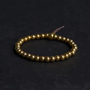 Copper brass Buddhist beaded bracelet with golden polished beads and brown leather tassel on dark background