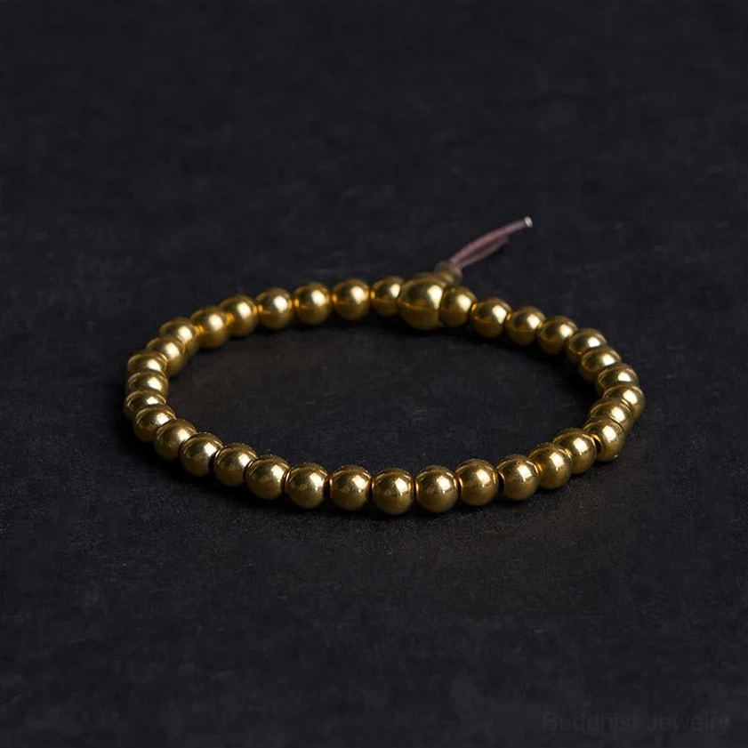 Copper brass Buddhist beaded bracelet with golden polished beads and brown leather tassel on dark background