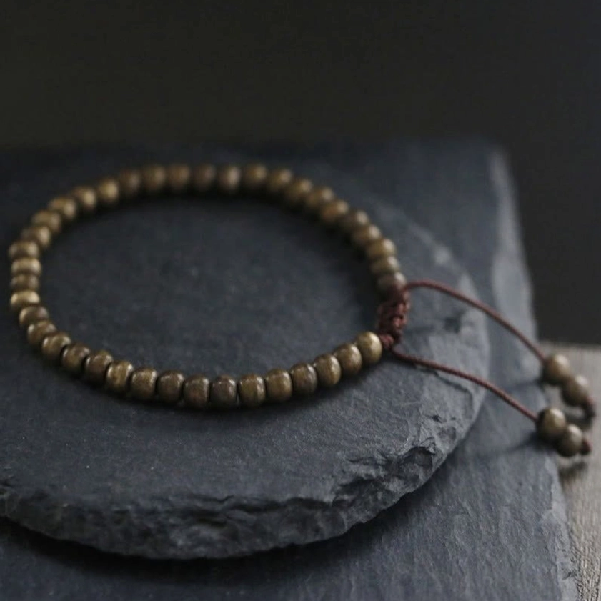 Double-strand copper bead bracelet three-quarter view, showing adjustable pull cords and matte bronze finish