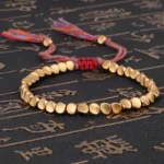 Matte gold copper beads Buddhist bracelet with multi-color braided cord and decorative tassels on dark background