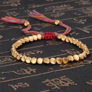 Matte gold copper beads Buddhist bracelet with multi-color braided cord and decorative tassels on dark background