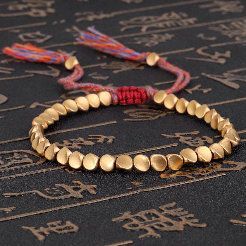 Matte gold copper beads Buddhist bracelet with multi-color braided cord and decorative tassels on dark background