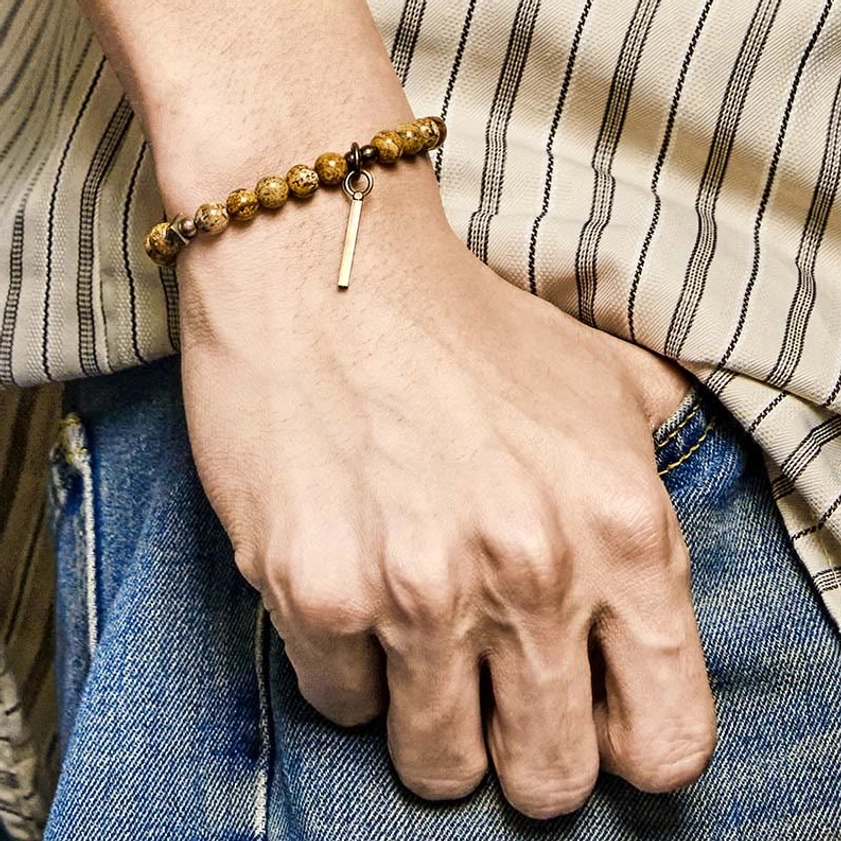 Men's copper and stone Buddhist bracelet worn on wrist with casual striped shirt outfit