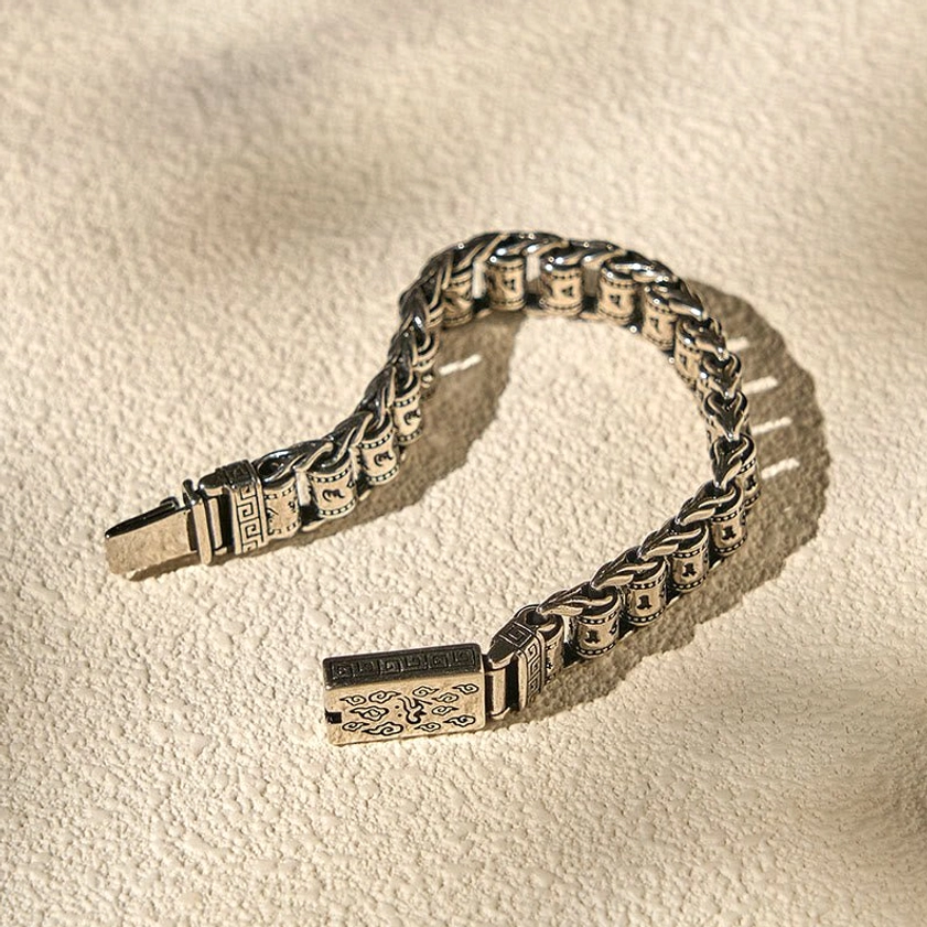 Low-angle side view of vintage bronze-tone copper Buddhist bracelet with engraved clasp on neutral fabric background