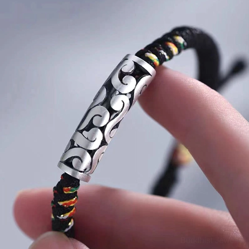 Close-up detail of copper cloud-engraved bead on black braided Buddhist string bracelet held in hand showing intricate cloud pattern
