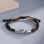 Copper auspicious cloud Buddhist string bracelet with cloud-patterned bead and black braided rope, three-quarter view on minimalist desktop