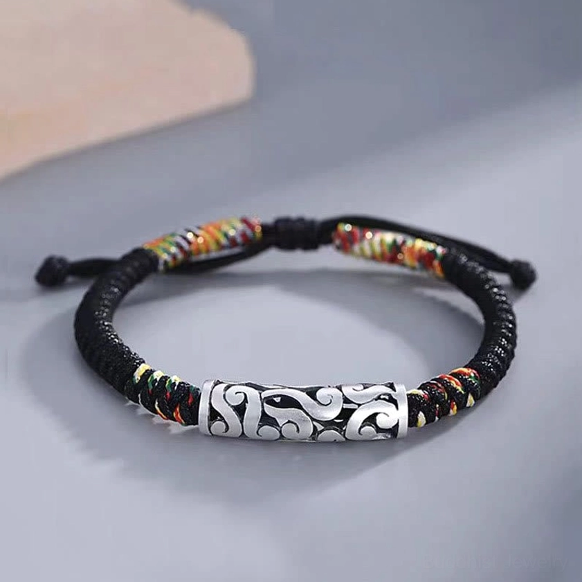 Copper auspicious cloud Buddhist string bracelet with cloud-patterned bead and black braided rope, three-quarter view on minimalist desktop