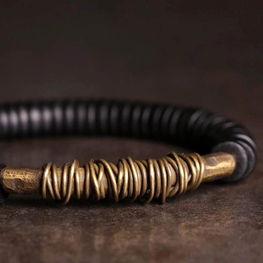 Detailed macro photograph of hand-coiled copper wire wrap with metal end caps and matte black ebony wood beads in Buddhist bracelet