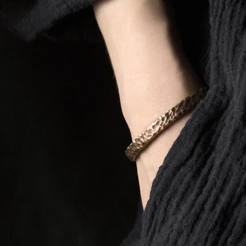 Copper wealth cuff bracelet worn on ankle with black linen clothing, demonstrating adjustable fit and textured finish
