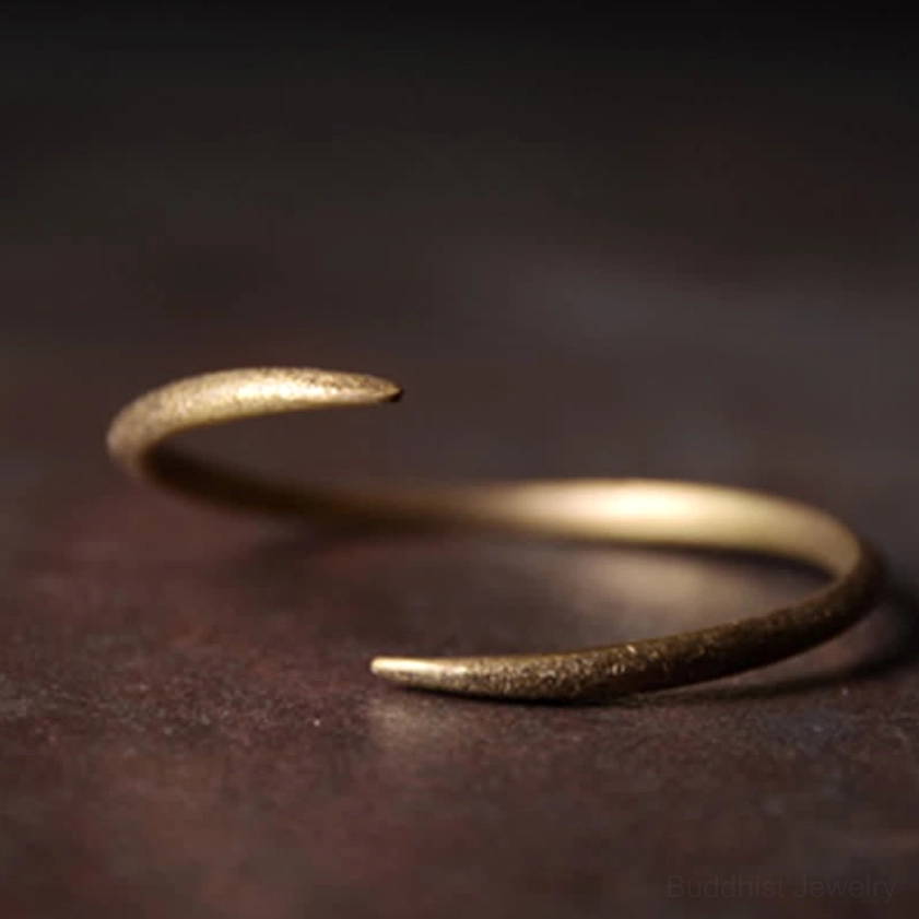 Single adjustable copper cuff bracelet with antique gold finish and open hook design on dark background