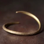 Adjustable copper cuff bracelet with matte textured finish on dark wooden surface, Buddhist spiritual jewelry for prosperity
