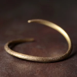 Adjustable copper cuff bracelet with matte textured finish on dark wooden surface, Buddhist spiritual jewelry for prosperity