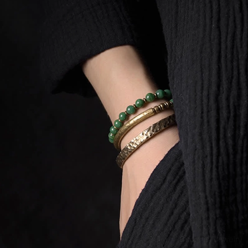 Multi-layer spiritual bracelet stack featuring hammered copper cuff paired with green beaded bracelet on wrist