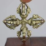 Handcrafted copper double dorje vajra held overhead close-up showing antique brass finish and carved scrollwork detail