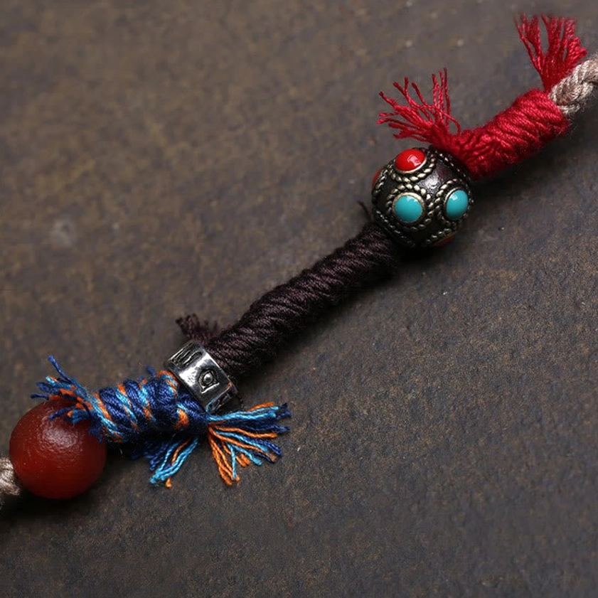 Close-up of copper dzi bead amulet pendant with red tassel and red agate stone ornament on dark background