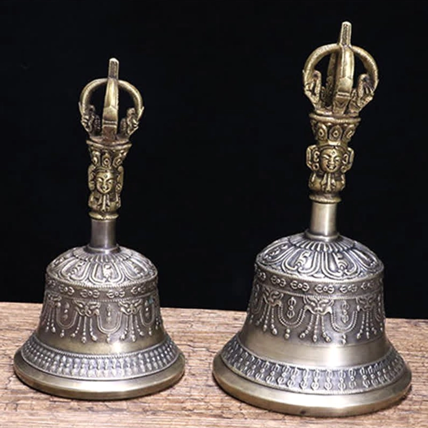 Pair of handcrafted copper meditation bells with bronze handle finials on wooden tabletop, showcasing floral embossing detail work