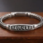 Copper Om Mani Padme Hum Buddhist bracelet with engraved mantra plaque and Vajra symbol, featuring vintage silver-tone braided chain on dark wooden background