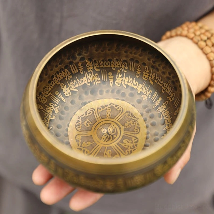 Handmade copper singing bowl with Sanskrit mantra engraving, top-down close-up view showing hammered texture and antique bronze finish