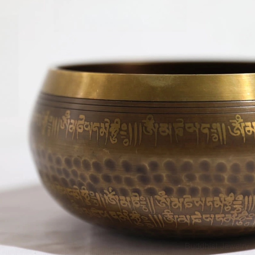 Studio close-up of handmade copper singing bowl with polished brass rim and traditional Buddhist script engraving