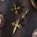 Handmade copper vajra dorje pendants displayed on dark fabric with lotus decoration, showing aged brass finish and traditional Buddhist ritual design