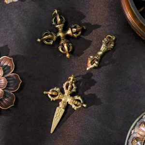 Handmade copper vajra dorje pendants displayed on dark fabric with lotus decoration, showing aged brass finish and traditional Buddhist ritual design