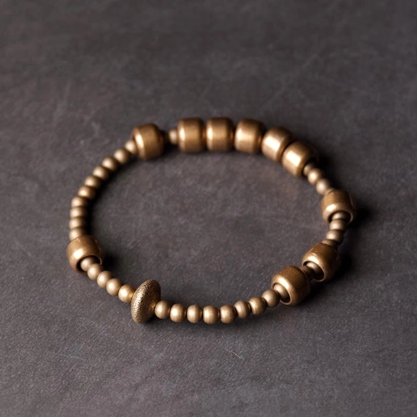 Vintage copper brass beaded bracelet overhead view showing mixed barrel bead design with textured focal bead for wealth and balance