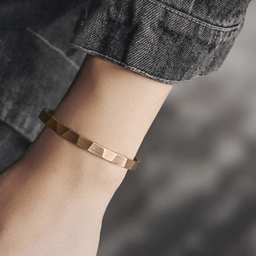 Adjustable copper prosperity bangle worn on wrist with denim cuff showing matte bronze hammered texture and open cuff design