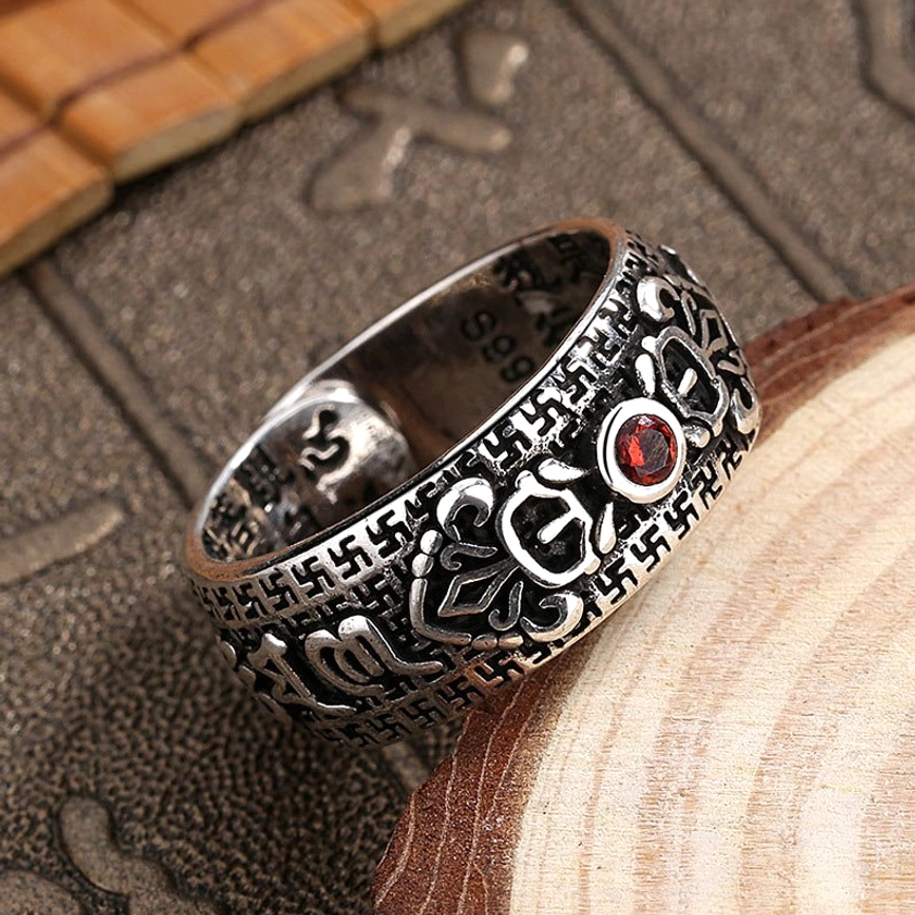 Low-angle view of handcrafted Buddhist wealth ring revealing inner hallmark 999 mark, religious motifs carving, and red ruby gemstone